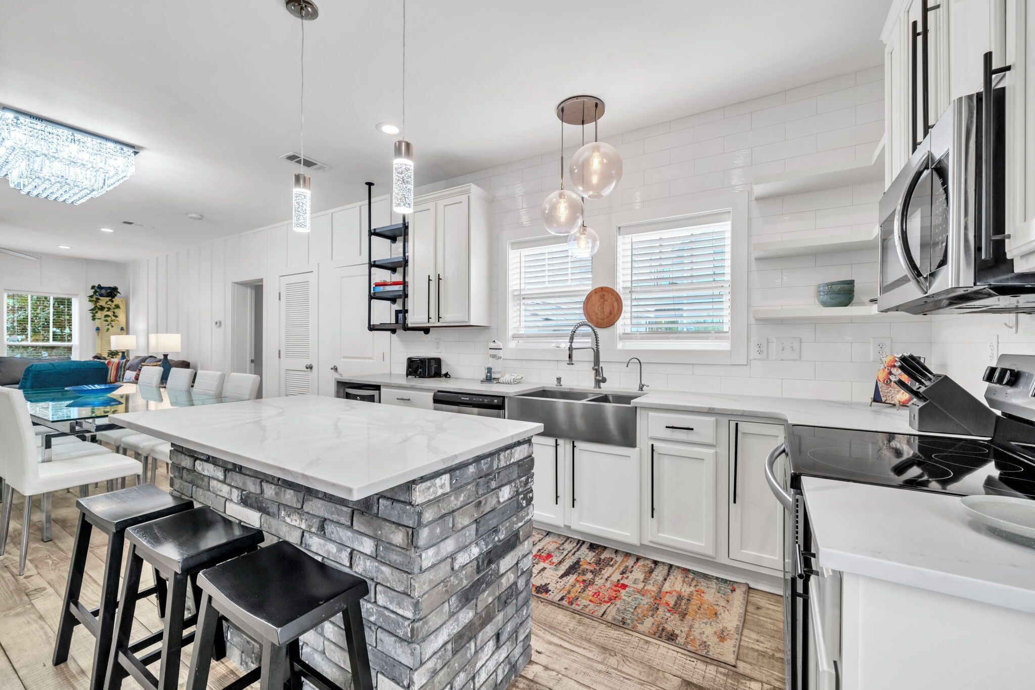 Een moderne keuken met witte kasten, een groot eiland met barkrukken, roestvrijstalen apparatuur en hanglampen.