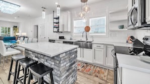 A modern kitchen with white cabinets, a large island with stools, stainless steel appliances, and pendant lighting.