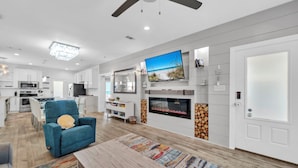 A modern living room with a flat-screen TV, a fireplace, and a dining area with a blue armchair.