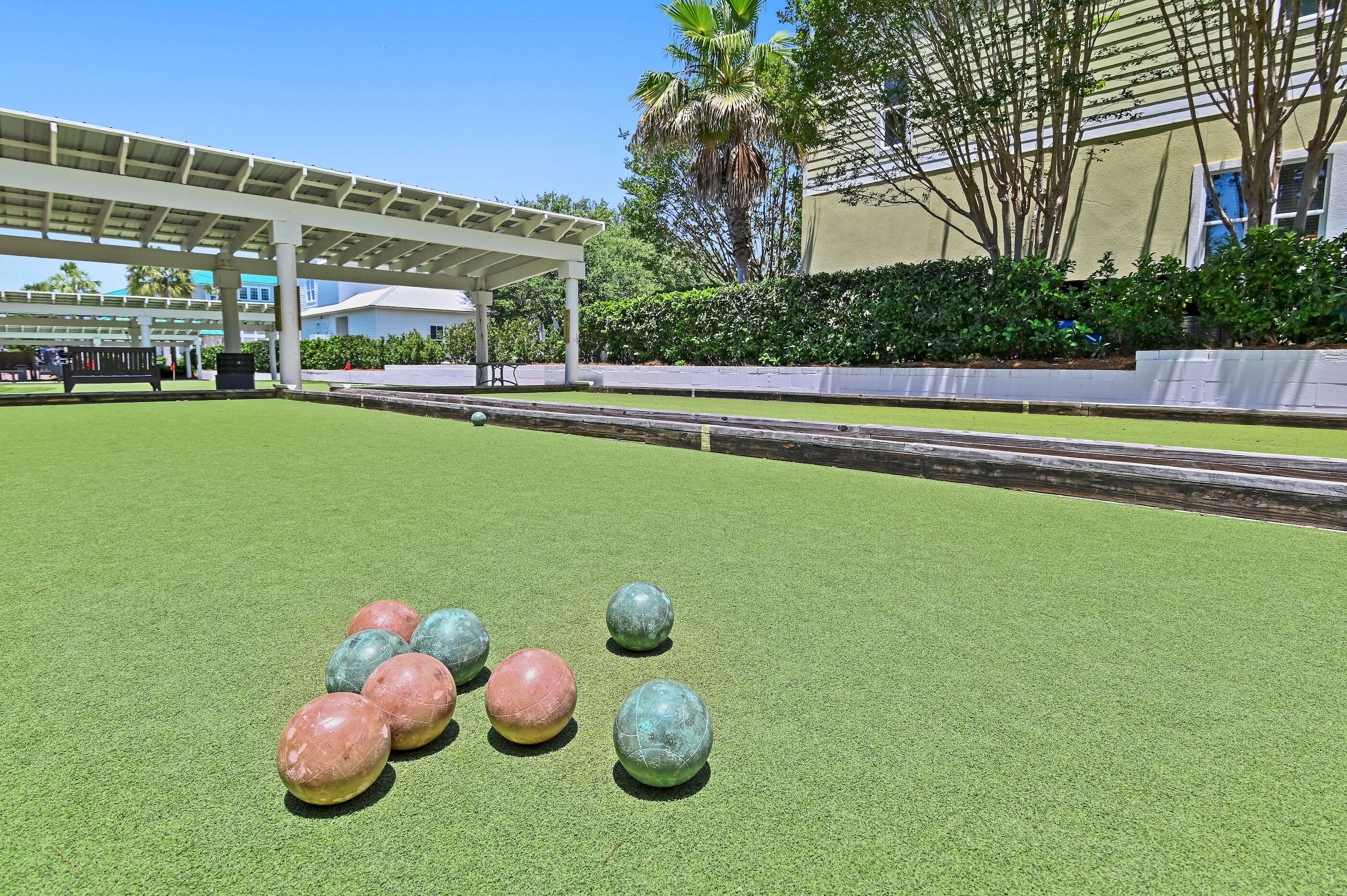 A green artificial turf area with colorful balls, a white pergola, and a building with a beige facade.