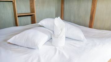 A neatly made bed with white linens and pillows, a wooden ladder, and a simple, unadorned wall.