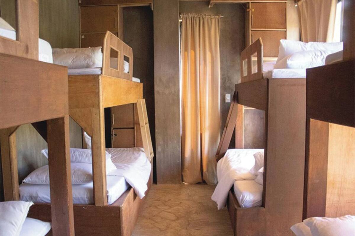 A dormitory room with bunk beds arranged in a central aisle, wooden walls, and a curtain separating the space.