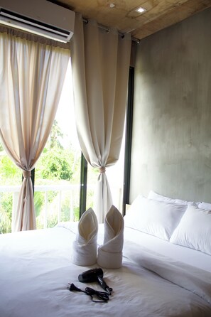 A hotel room with a bed, white curtains, and a window with a view of greenery. - Ohayo Siargao (General Luna)