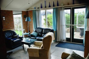 Een woonkamer met een bakstenen muur, een leren bank in het zwart, een rieten fauteuil en een salontafel.