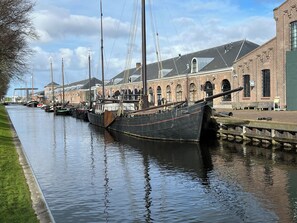 Een gracht met verschillende boten afgemeerd langs een bakstenen gebouw met rondboogvensters.