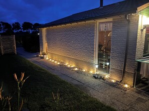 Een bakstenen gebouw met een raam, een deur en een pad verlicht door grondspots.