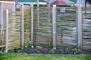 Een houten hekwerk met een rankenstructuur, omgeven door een tuin met narcissen.