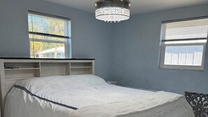 A bedroom with a bed, a chandelier, and two windows. - Charming 2-bedroom house in Charlotte Harbor, walk to restaurants & shopping (Port Charlotte)