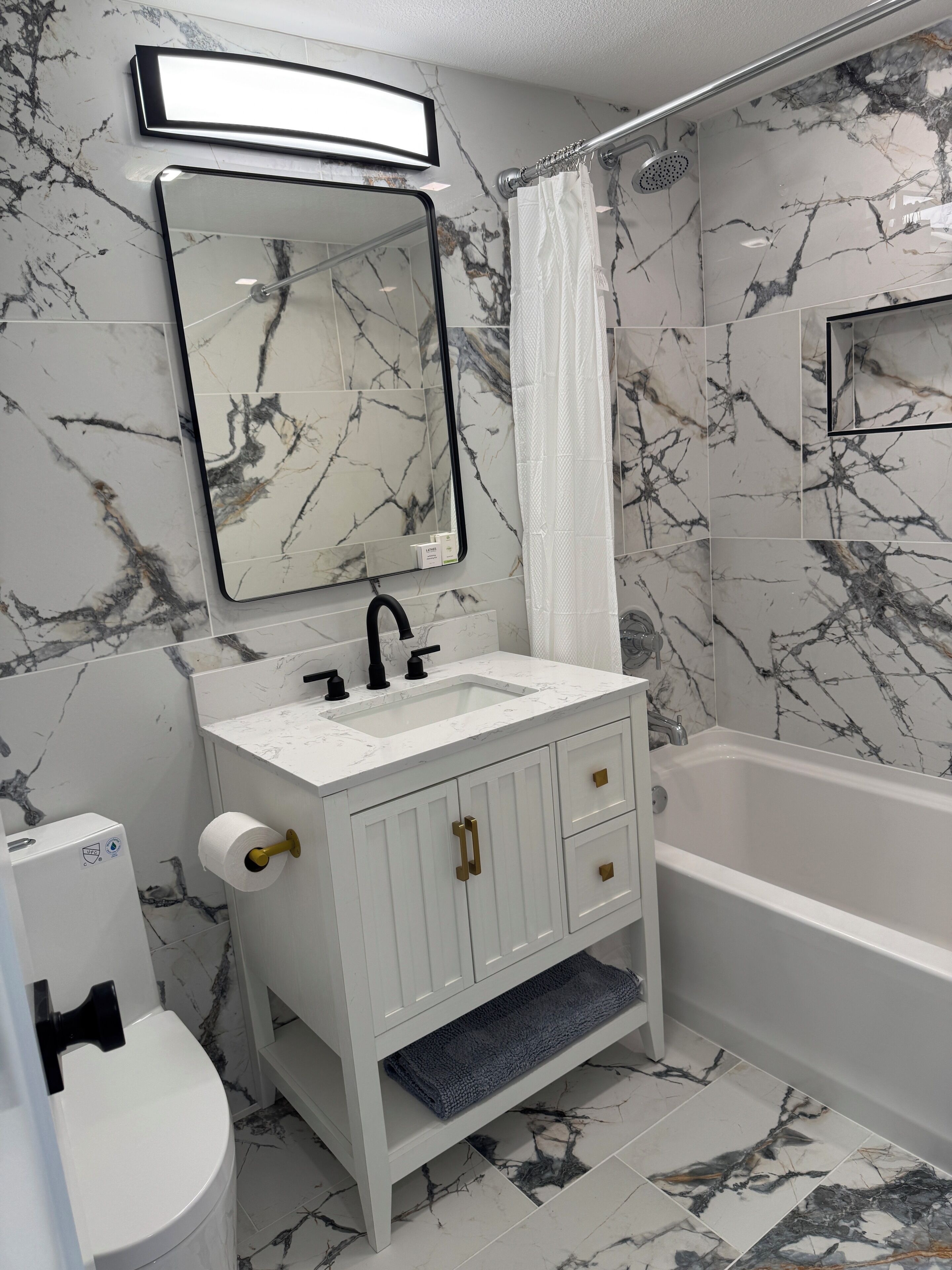 Une salle de bain avec un pare-baignoire en marbre, un lavabo blanc, un miroir, des toilettes et une baignoire.
