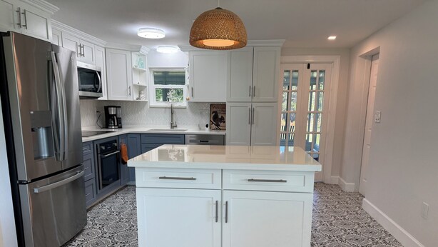 A modern kitchen with white cabinetry, a stainless steel refrigerator, a microwave, and a patterned floor. - Charming 2-bedroom house in Charlotte Harbor, walk to restaurants & shopping (Port Charlotte)