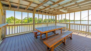 An outdoor wooden deck with a picnic table and benches, overlooking a body of water.
