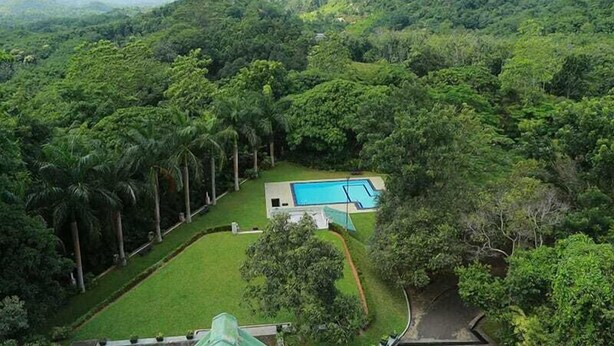 Un paisaje exuberante y verde con una piscina y un edificio rodeado de densa vegetación y colinas.