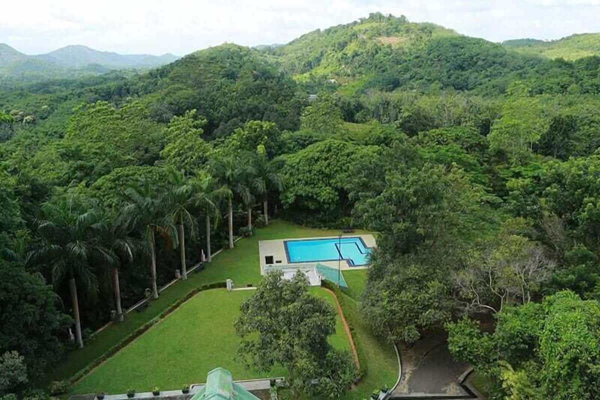 A lush green landscape with a swimming pool and a building surrounded by dense vegetation and hills.