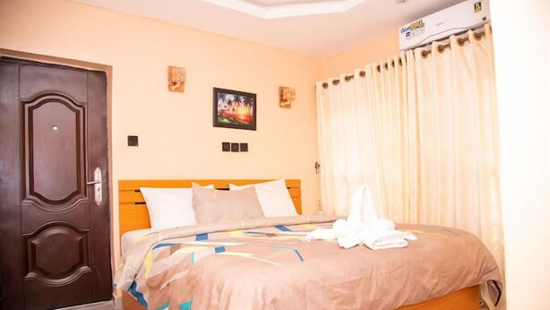 A hotel room with a wooden bed, beige walls, and a large window with curtains. - Dopad Hills Hotel and Suites (Ibadan)