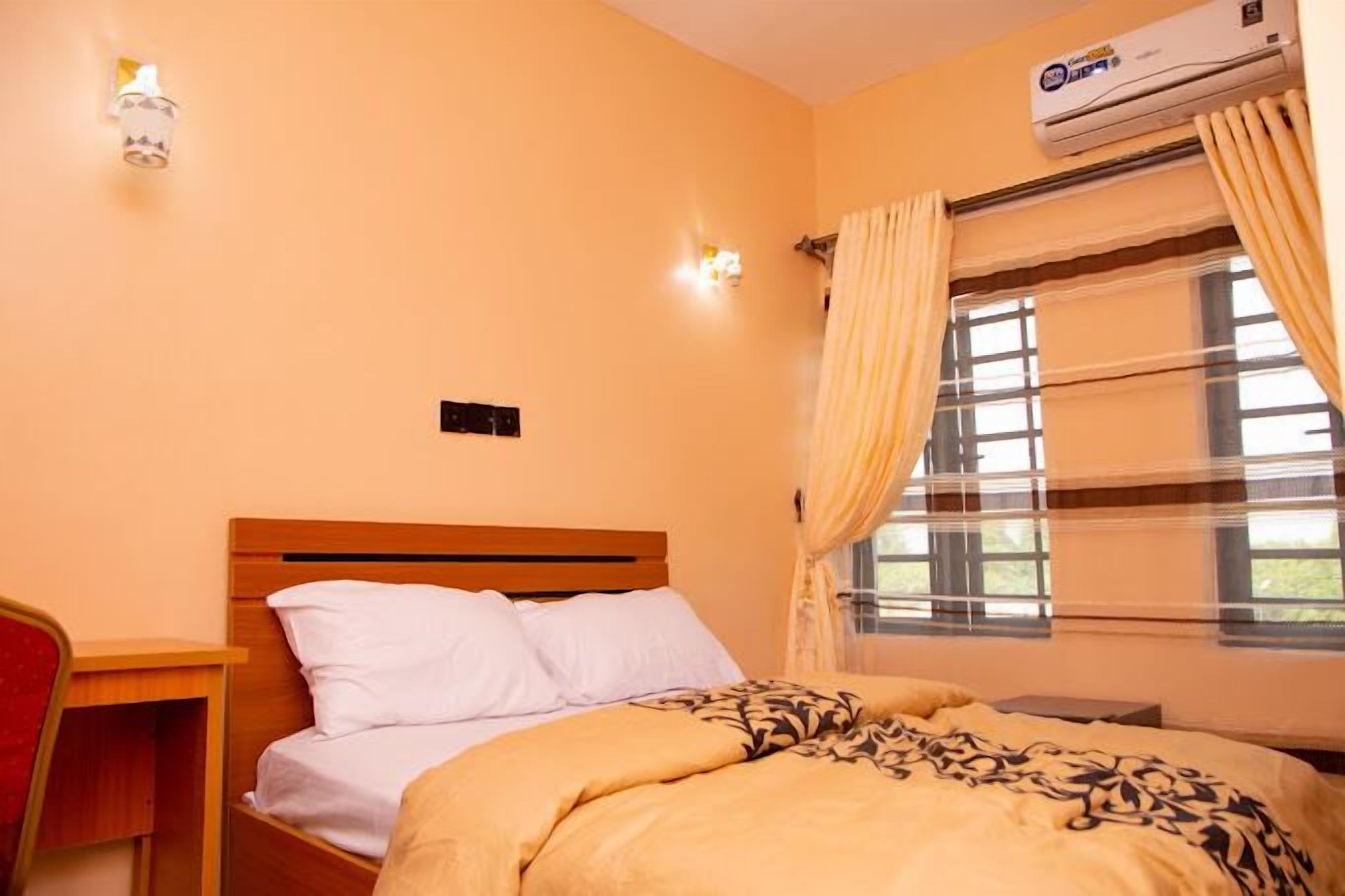 Une chambre à coucher comprenant un lit, une table de chevet, une lampe et un appareil de climatisation.
