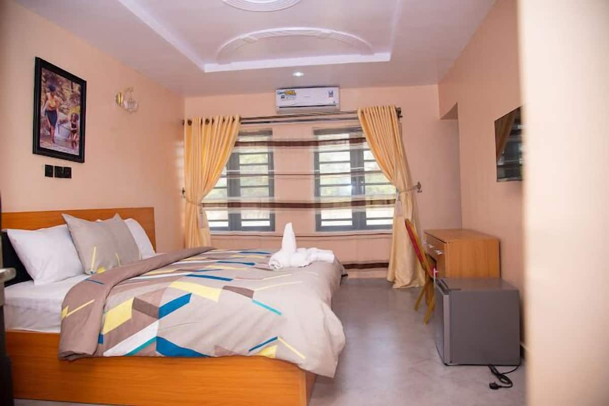 Una habitación de hotel con cama, escritorio, aire acondicionado y ventana con cortinas.