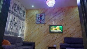 A living room with a marble wall, a chandelier, a television, and two sofas. - Dopad Hills Hotel and Suites (Ibadan)