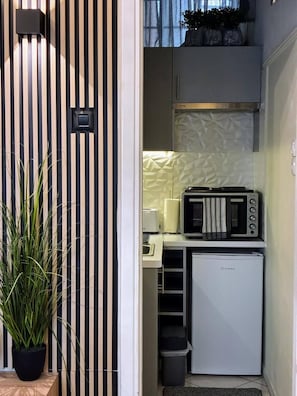 A compact kitchenette with a microwave, toaster, and refrigerator, a potted plant, and a striped wall.
