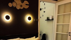 Quarto de hotel com cama, cadeira, porta e luminária fixada na parede.