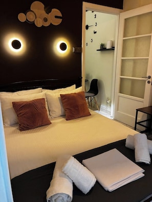 A hotel room with a bed, a chair, a door, and a wall-mounted light fixture.