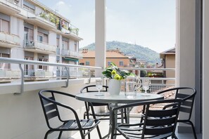 Un balcon avec une table ronde, des chaises en métal noir et un pot de fleurs contenant des fleurs jaunes.