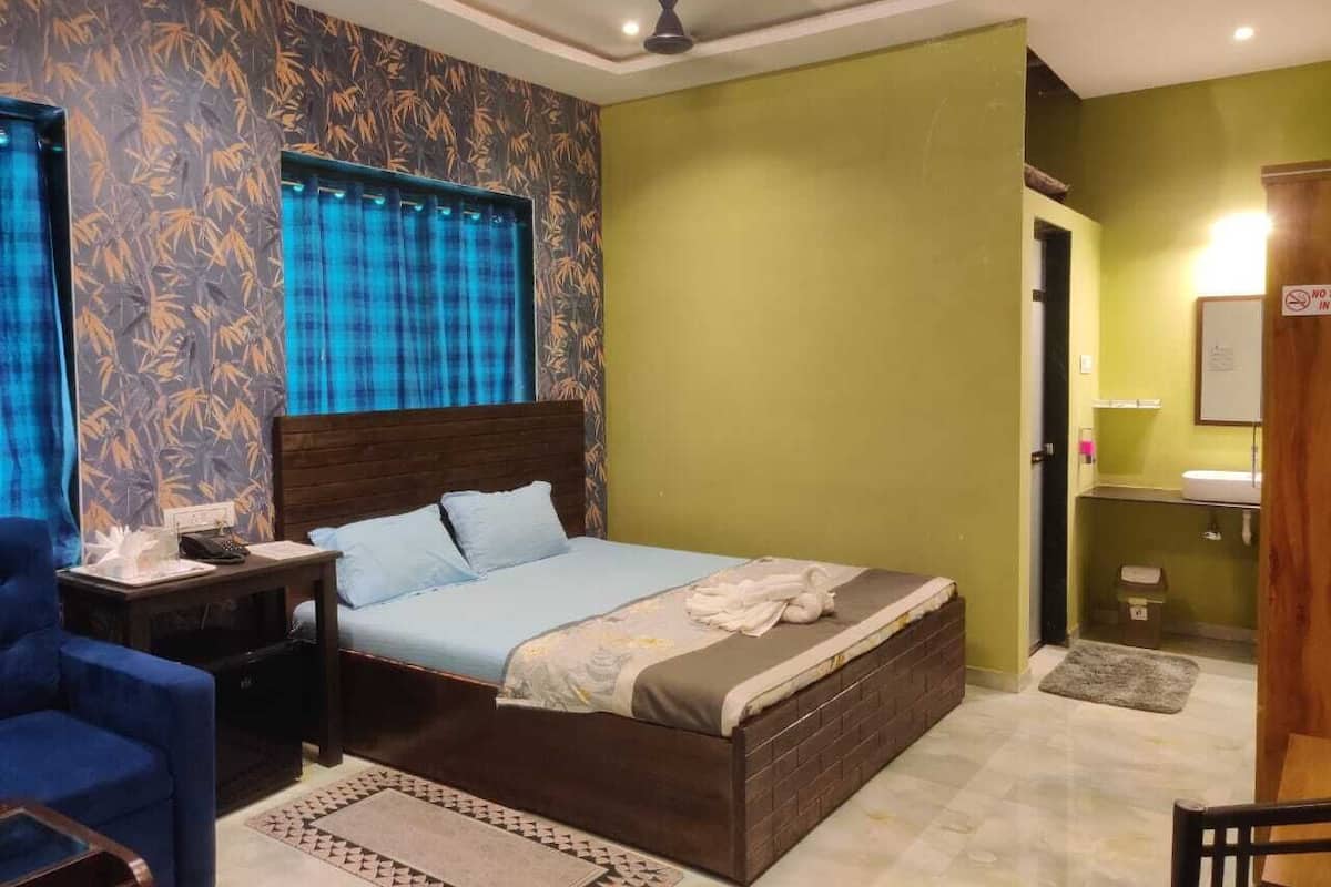 A bedroom with a bed, a nightstand, a chair, and a bathroom with a sink and mirror.