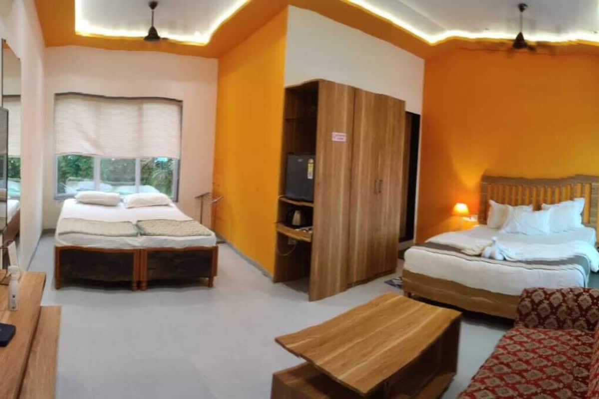 A hotel room with two beds, a wooden wardrobe, a red patterned sofa, and a wooden table.