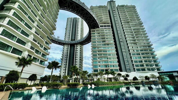 A modern high-rise building with a curved bridge structure, a swimming pool with swan decorations, and lush greenery. - 1-bedroom apartment in marvelous Kuala Lumpur with free WiFi + Netflix (Wilayah Persekutuan)
