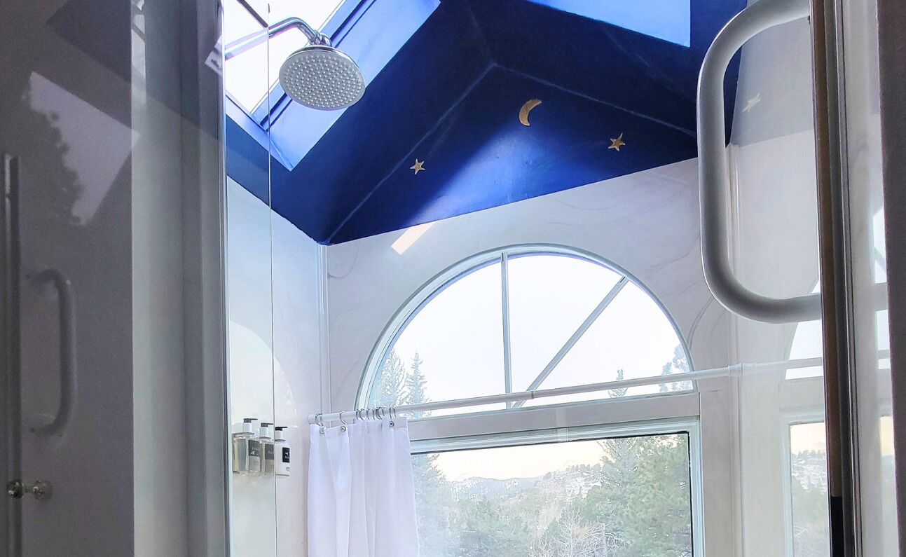 Une salle de bain dotée d’un puits de lumière, d’une grande fenêtre en arc de cercle et d’une douche.