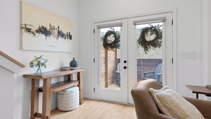 Una sala de estar con una mesa de madera, un sofá, una puerta adornada con un adorno y un cuadro de un paisaje urbano en la pared.