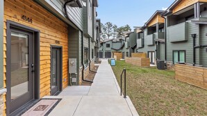 Una hilera de edificios de apartamentos modernos con revestimiento de madera y gris, un camino de hormigón y una zona ajardinada.