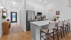 Una cocina moderna con armarios blancos, electrodomésticos de acero inoxidable y una isla central con taburetes de bar.