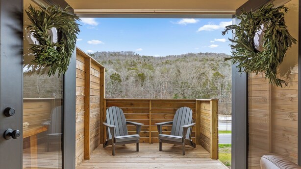 Una terraza de madera con dos sillas Adirondack orientadas a una vista panorámica de una ladera boscosa.