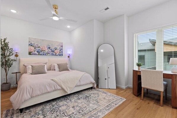 Un dormitorio con una cama, un escritorio, una silla, un espejo grande y un cuadro en la pared.