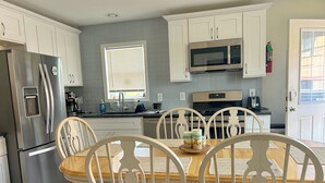 Una cocina moderna con armarios blancos, electrodomésticos de acero inoxidable y una zona de comedor con una mesa y sillas de madera.