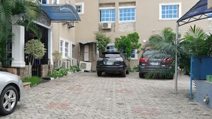 A paved driveway leading to a building with a stone facade, a car parked on the left, and another car parked on the right. - Ladalob Royal Suites (Ibadan)
