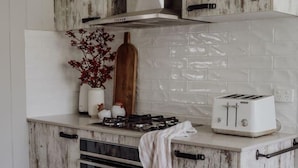Uma cozinha com design rústico, com ladrilho branco na parede, bancada de madeira, fogão e torradeira.