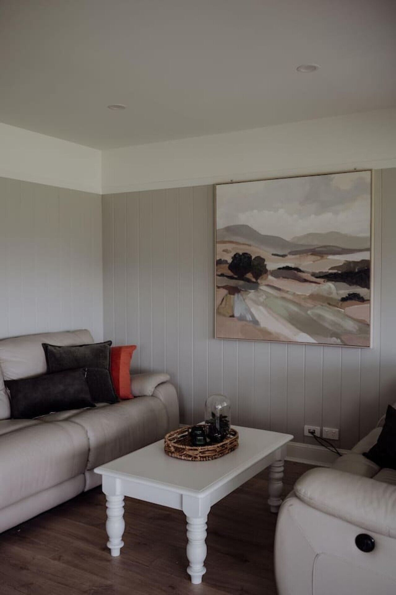 Ein Wohnzimmer mit einem beigen Sofa, einem weißen Couchtisch und einem Bild an der Wand.