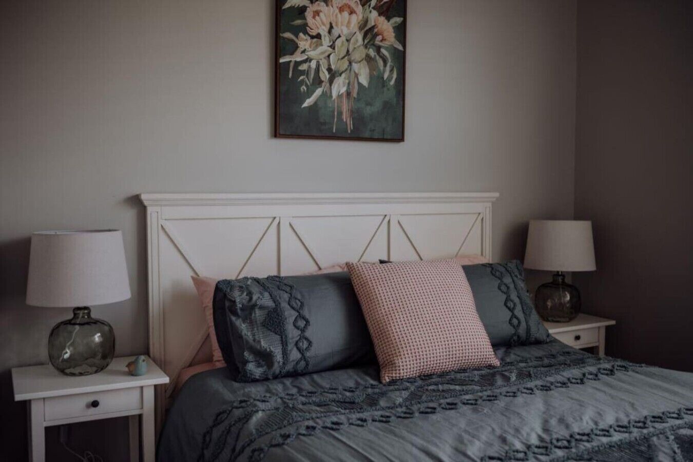 Een slaapkamer met een bed, twee nachtkastjes, lampen, een schilderij en een hoofdbord.