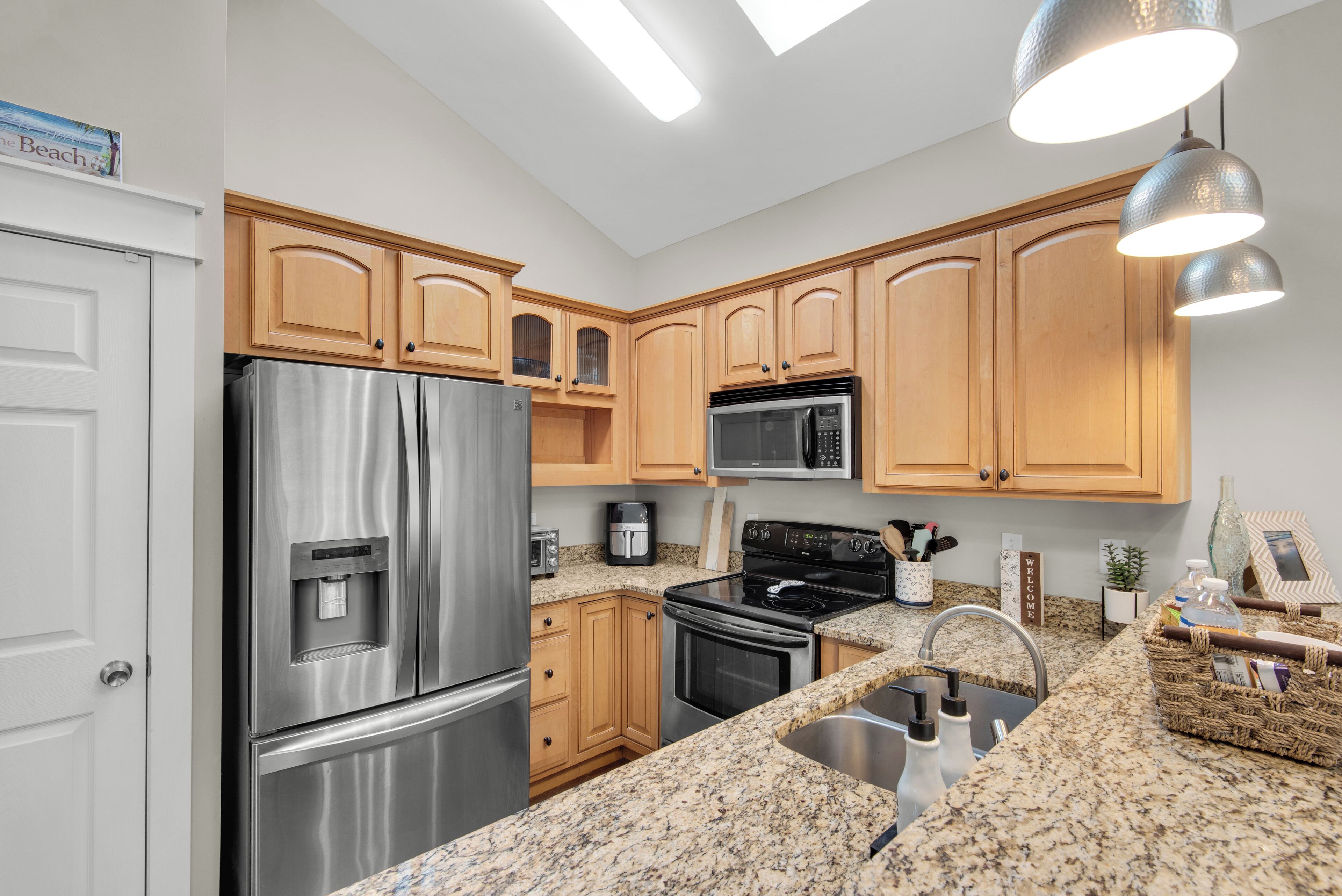 A modern kitchen with stainless steel appliances, wooden cabinets, granite countertops, and pendant lighting.