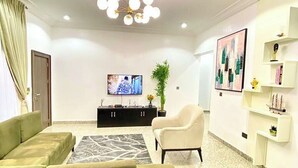 Una sala de estar moderna con un sofá modular, un sillón blanco, un mueble de entretenimiento negro y una planta decorativa.