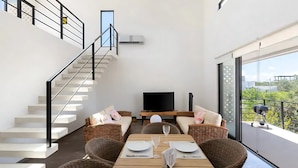 A modern living room with a dining area, a flat-screen TV, and a balcony with a grill. - Tulum Penthouse Retreat With Private Pool and Stunning Sunset Views (Tulum)