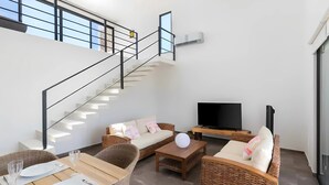 A modern living area with a staircase, wicker furniture, a flat-screen TV, and a dining table set. - Tulum Penthouse Retreat With Private Pool and Stunning Sunset Views (Tulum)