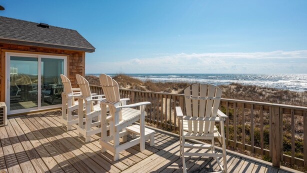 A wooden deck with white Adirondack chairs overlooking a beach. - Oceanfront charm, heated pool, hot tub, dog friendly, 4 bed 3.5 bath (Frisco)