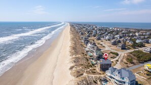 An aerial view of a coastal residential area with houses along the beach, a clear sky, and a marked location. - Oceanfront charm, heated pool, hot tub, dog friendly, 4 bed 3.5 bath (Frisco)