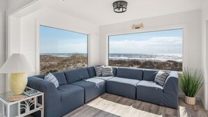 A modern living room with a large sectional sofa, a small side table, and a view of the beach. - Oceanfront charm, heated pool, hot tub, dog friendly, 4 bed 3.5 bath (Frisco)