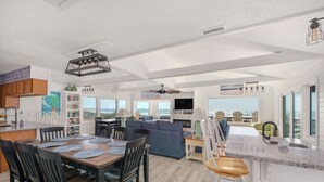 A spacious living area with a dining table, sofas, and a kitchen area with a view of the ocean. - Oceanfront charm, heated pool, hot tub, dog friendly, 4 bed 3.5 bath (Frisco)