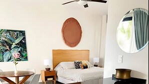 A modern hotel room with a central island, a bed with striped bedding, a round mirror, and a large water dispenser. - Discover Your Tulum Sanctuary Stylish Studio in Vibrant La Veleta! (Tulum)