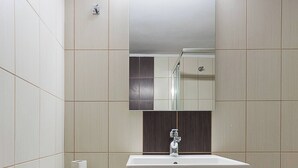 A bathroom with a white sink, a mirror above it, and a tiled wall. - Creta Beachfront Apartment B for 2 persons by MPS (Paralia Fodele)