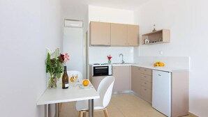 A compact kitchen with a white table, a white chair, and a small countertop with a sink. - Creta Beachfront Apartment B for 2 persons by MPS (Paralia Fodele)